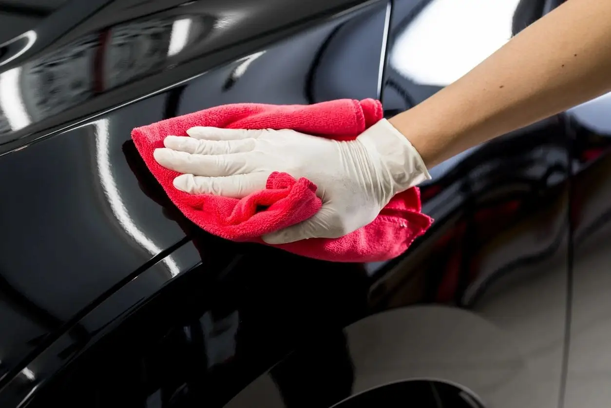 Technician polishing a glossy black car panel after dent and scratch repair